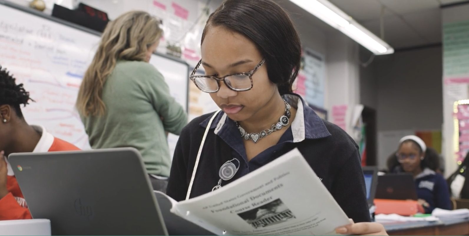 A New Orleans student reads a U.S. Government course reader beside a laptop